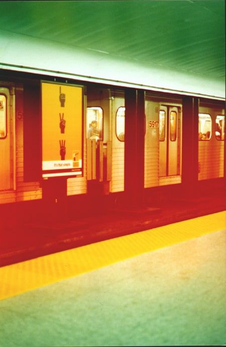 Cross-processed photograph of a subway train stopped at a platform with a yellow edge strip, glowing in red, orange and green.